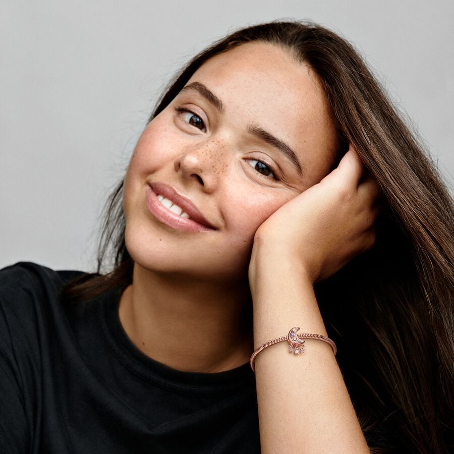 Star & Crescent Moon Charm - Pandora West Africa Charms Add celestial sparkle to any look with the Star & Crescent Moon Charm. Finished in 14k rose gold plating, the charm has been carefully detailed by hand with rows of cubic zirconia and cut-out star and circle shapes. Microbeads decorate the edges and asymmetric stars with stones and microbeads dangle from the sides. The cosmic charm is engraved with the message "Dream big" to remind you to always reach for the stars. (789643C01)  