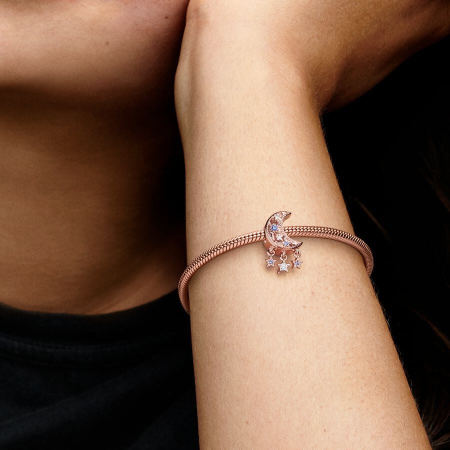 Star & Crescent Moon Charm - Pandora West Africa Charms Add celestial sparkle to any look with the Star & Crescent Moon Charm. Finished in 14k rose gold plating, the charm has been carefully detailed by hand with rows of cubic zirconia and cut-out star and circle shapes. Microbeads decorate the edges and asymmetric stars with stones and microbeads dangle from the sides. The cosmic charm is engraved with the message "Dream big" to remind you to always reach for the stars. (789643C01)  