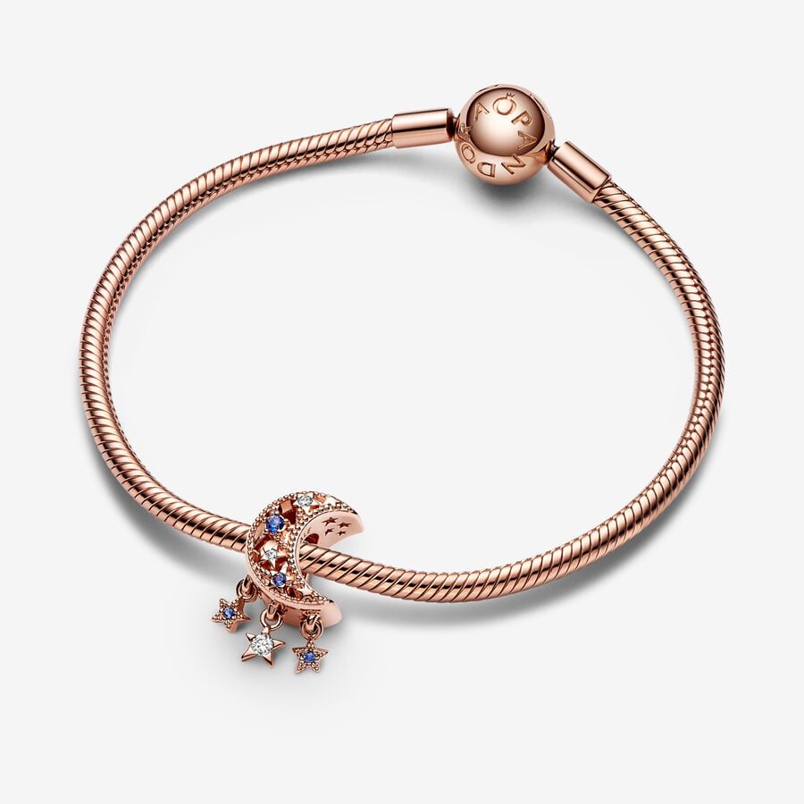 Star & Crescent Moon Charm - Pandora West Africa Charms Add celestial sparkle to any look with the Star & Crescent Moon Charm. Finished in 14k rose gold plating, the charm has been carefully detailed by hand with rows of cubic zirconia and cut-out star and circle shapes. Microbeads decorate the edges and asymmetric stars with stones and microbeads dangle from the sides. The cosmic charm is engraved with the message "Dream big" to remind you to always reach for the stars. (789643C01)  